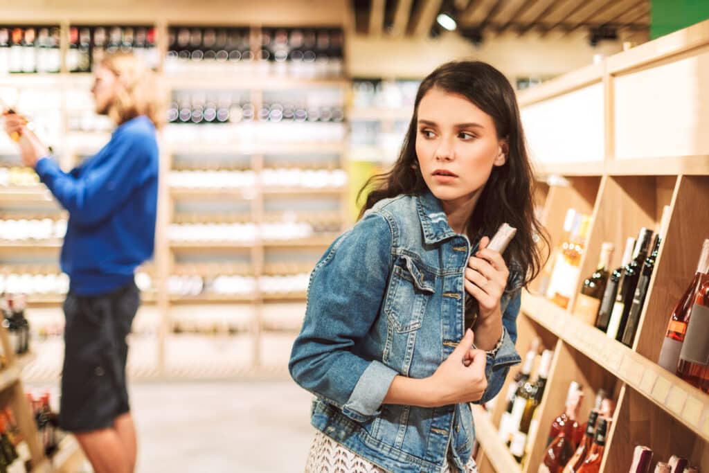 Young frightened woman in denim jacket hiding alcohol in her jacket