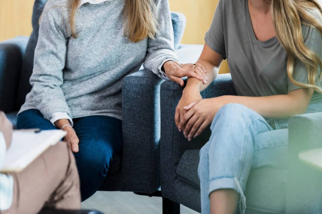 An mother touches her daughter's arm while talking with a therapist during a family counseling session.