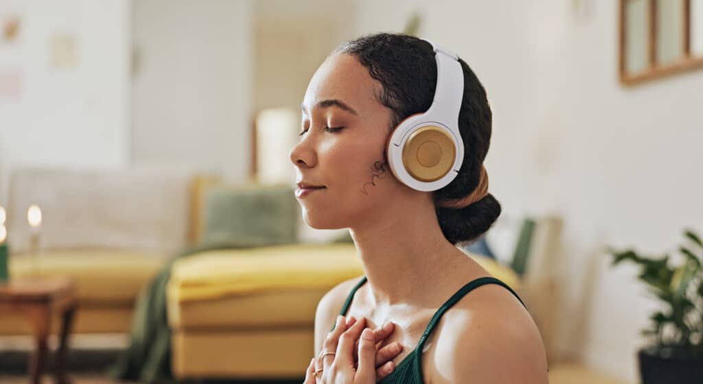 Woman, meditation and yoga in headphones listening to calm music, holistic somatic therapy exercise to regulate emotions and find peace in living room. 