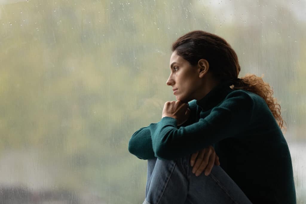 Side view frustrated thoughtful woman looking out rainy window in distance alone, dealing with depression and struggling with emotional dysregulation 