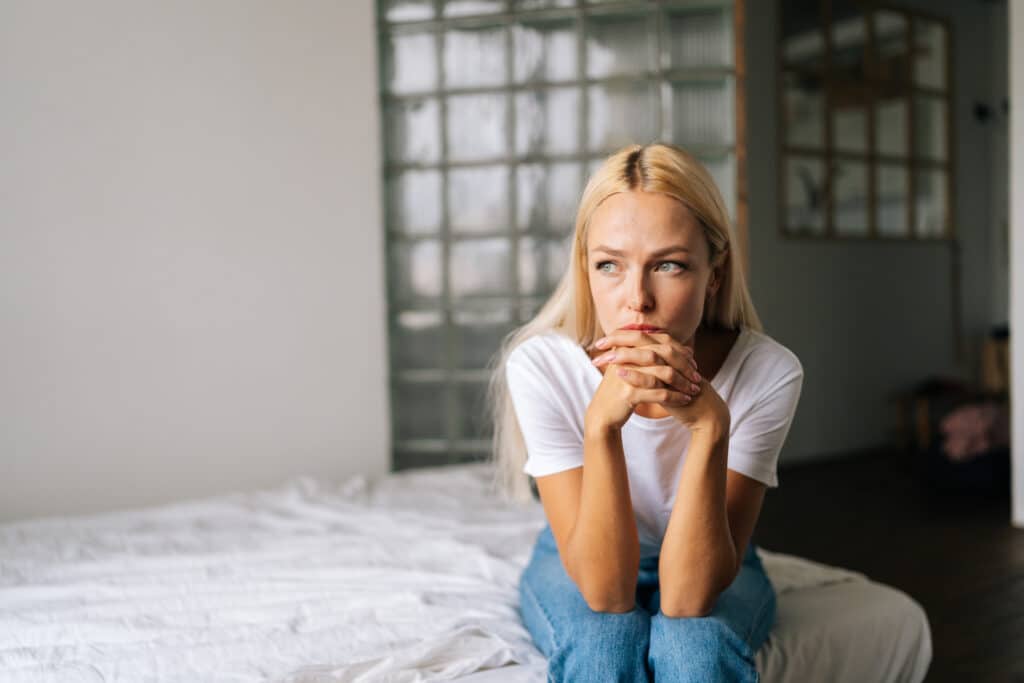 Portrait of depressed woman sitting alone at home and looking away with sad expression holding hands on chin, deep thoughts feeling lonely. Frustrated blonde female pondering make difficult choice.