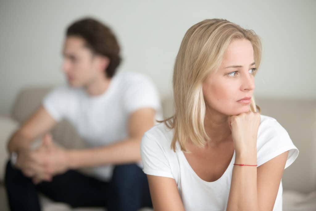 Serious sad woman with her partner in the background, struggling in her relationship from unresolved complex trauma